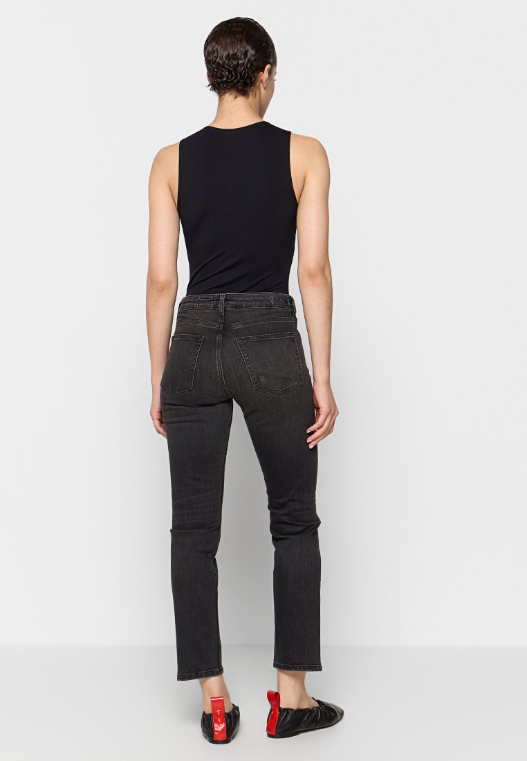 Czarna bluzka na ramiączkach, czarne dżinsy o prostym nogawce z średnim stanem oraz czarne buty z czerwonymi akcentami. Widok z tyłu prezentujący dopasowanie i szczegóły.