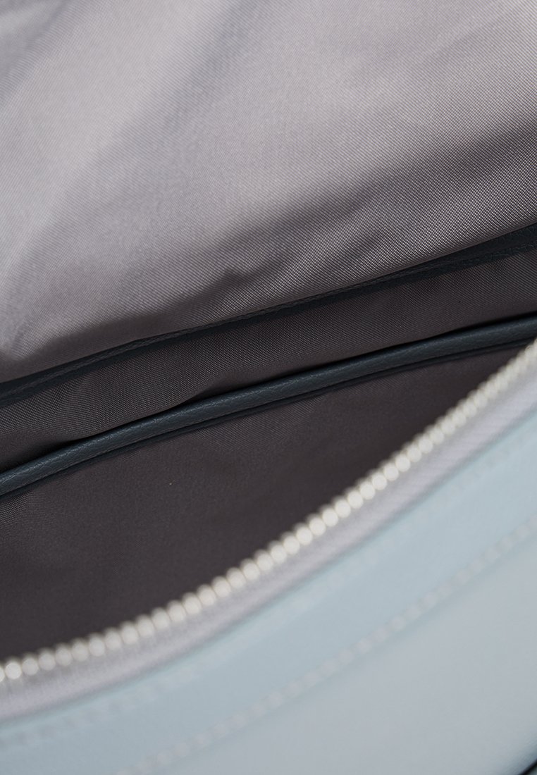Helles blaues Tascheninnere mit grauem Stofffutter, ausgestattet mit einem Reißverschluss und einer flachen Taschennaht zur Organisation. Glatte Textur im gesamten Inneren.