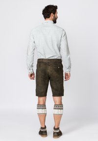 Braune Lederhosen-Shorts mit strukturiertem Finish, kombiniert mit einem karierten Langarmhemd mit Ellbogenpatches und dekorativen Kniewärmern.