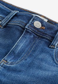 Blå denimjeans med knappstängning, kontrasterande sömmar och en lätt blekt textur. Inkluderar bältesloopar och framfickor.