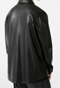 Chaqueta de cuero negro con una textura suave, corte relajado y un cuello clásico. Cuenta con mangas largas y un dobladillo curvado en la parte de atrás.