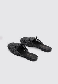 Chaussures slip-on noires en lin avec un design ouvert, un talon plat et une surface texturée ornée de motifs floraux. Semelle en caoutchouc pour une meilleure adhérence.