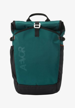 Teal and black roll-top backpack with front buckle, side pockets, top handle, and subtle "AEVOR" branding on front panel.