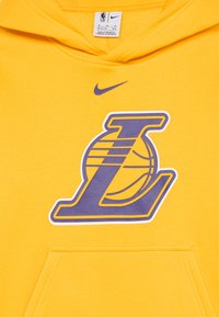 Žuta hudica od mekog materijala sa velikim ljubičastim "L" logotipom ispod kojeg se nalazi dizajn košarkaške lopte i malim ljubičastim Nike swooshom.