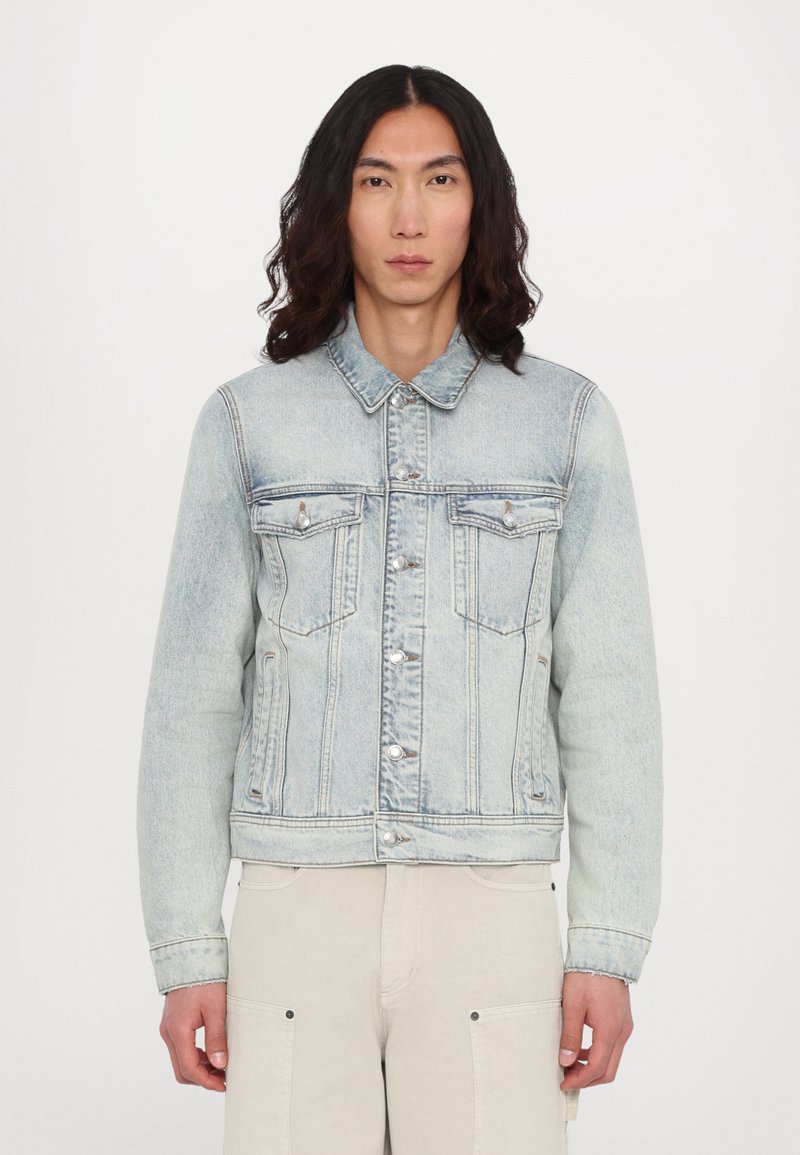 Light blue denim jacket with long sleeves, two chest pockets, button closure, and a faded wash. Smooth texture with minimal hardware accents.