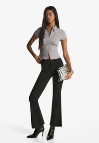 Tætsiddende gråstribet kortærmet skjorte med en lynlås foran, parret med sorte smækkede bukser og en skinnende sølv clutch. Sorte stiletto hæle.