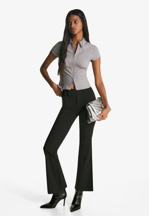 Tætsiddende gråstribet kortærmet skjorte med en lynlås foran, parret med sorte smækkede bukser og en skinnende sølv clutch. Sorte stiletto hæle.