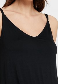 Top negro sin mangas con tirantes finos, escote en V y corte relajado. Elaborado en una tela suave y ligera con una textura lisa.