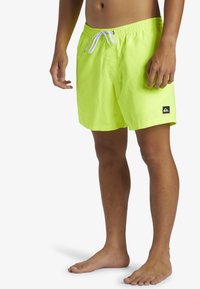 Bañador neon amarillo con cintura elástica y cordón, que presenta un parche de logo negro en la pierna izquierda. Material suave y ligero.