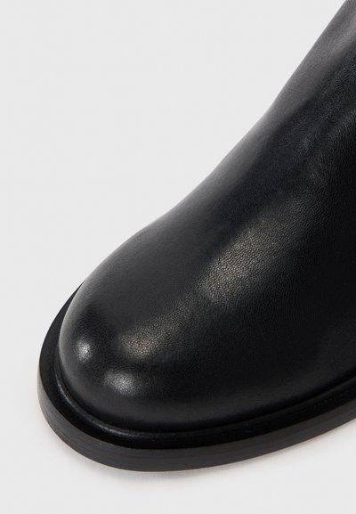 Stivale alla caviglia in pelle nera con punta arrotondata, texture liscia, brillantezza sottile e suola in gomma nera robusta e a profilo basso.