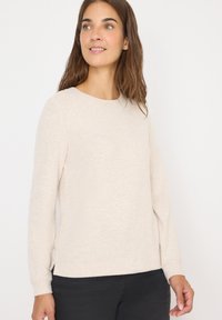 Pull en beige à manches longues avec un col rond, texture douce et fentes sur l'ourlet latéral, associé à un pantalon sombre.