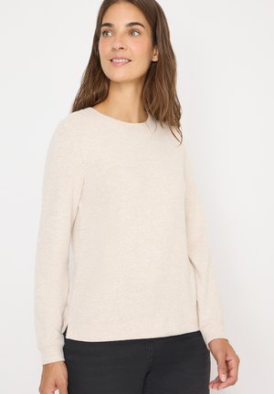 Maglione beige a maniche lunghe con scollo rotondo, texture morbida e spacchi all'orlo laterale, abbinato a pantaloni scuri.