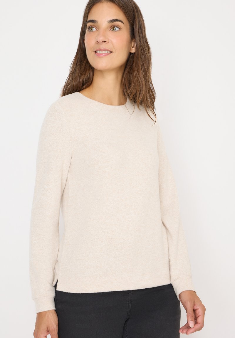 Pull en beige à manches longues avec un col rond, texture douce et fentes sur l'ourlet latéral, associé à un pantalon sombre.