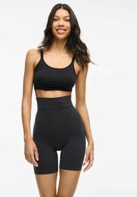 Set atletico nero composto da un top corto e pantaloni corti a vita alta, realizzati in tessuto liscio e elasticizzato con cuciture minime.