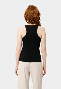 Top sin mangas negro de canalé con un diseño ajustado, escote redondo y tirantes anchos, combinado con pantalones de pierna ancha en un tono beige claro.