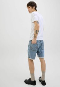 Light blue denim shorts with rolled hem, worn with a plain white t-shirt. Casual black shoes and beige socks, back view displayed.