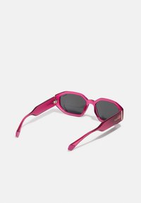 Gafas de sol rosas con un diseño geométrico, con lentes oscuros, montura gruesa y acentos metálicos en los laterales.