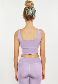 Laventeli urheiluinen crop-top, jossa on sileä pinta ja leveät hihnat, yhdistettynä yhteensopiviin korkeavyötäröisiin legginseihin. Molemmissa on tiivistetty muotoilu.