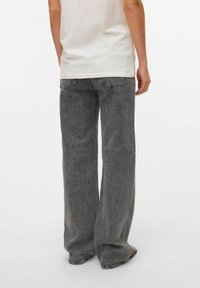 Jeans anchos grises con una textura desgastada, diseño de cinco bolsillos y costuras en contraste, combinados con una camiseta blanca sencilla.