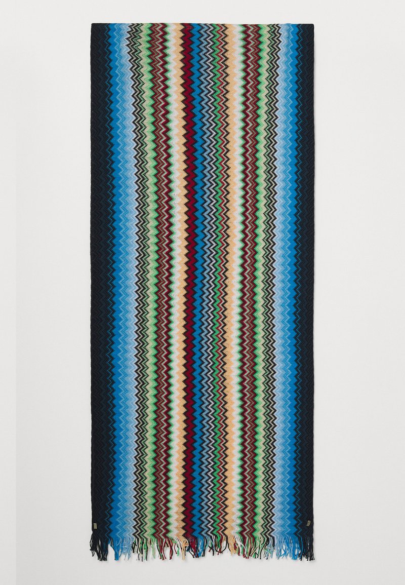 Woven blanket featuring zigzag patterns in blue, green, red, and cream, with fringe edges and a textured surface.