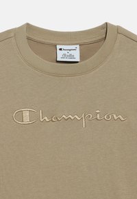 Μπεζ βαμβακερό φούτερ με στρογγυλή λαιμόκοψη και κεντημένο λογότυπο "Champion" σε αντίθετο χρώμα. Ορατές ετικέτες στο εσωτερικό του γιακά.