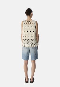 Top de ganchillo en crema con patrones recortados y acentos metálicos. Combinado con pantalones cortos de mezclilla azul claro con bordes deshilachados.