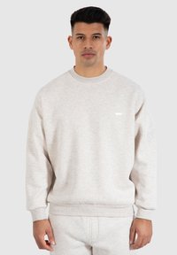 Sudadera gris clara de tela suave con cuello redondo, puños y dobladillo acanalados. Presenta un pequeño y sutil logo en el pecho.