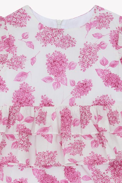 Lett bomullskjole med hvit bakgrunn, med et rosa blomsterdesign og volanger langs kanten og ermene. Glidelås bak.