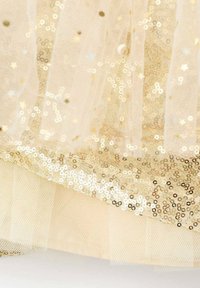 Tissu en sequins dorés avec une superposition de tulle transparent. Présente des sequins circulaires brillants, une texture douce et des détails en couches au bas.