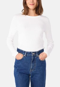 Witte langwerpige top gecombineerd met hoge taille blauwe spijkerbroek. De top heeft een ronde halslijn en aansluitende mouwen. Klassieke spijkerstof zichtbaar.