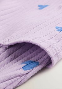 Violets tekstūru audums ar vertikālām svītrām un ziliem sirds rakstiem. Iezīmē mīkstu, pūkainu iekštelpu un rullētu apmali.