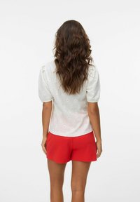 Hvit bluse med puffede ermer som har et diamant øyelet mønster, paret med røde shorts, som viser en jevn tekstur og solide farger.