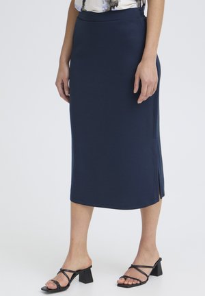 Mujer vistiendo una falda lápiz midi azul marino combinada con sandalias negras de tacón, de pie contra un fondo claro y sencillo.