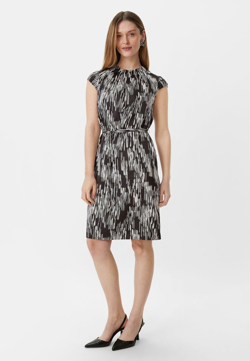 Schwarz-weiß gemustertes Kleid mit kurzen Ärmeln, taillierter Taille, knielanger Schnitt und glatter Textur, kombiniert mit schwarzen spitzen Absätzen.