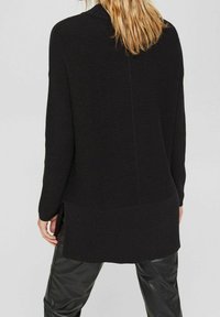 Svart långärmad stickad tröja med texturerad ribbad tyg, sidoflikar och avslappnad passform, tillsammans med glänsande svarta byxor.