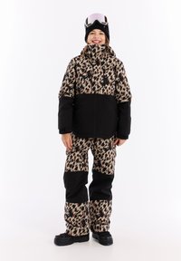 Beige en zwarte sneeuwjas met luipaardpatroon, gecombineerd met bijpassende broek. Kenmerken zijn een hoge kraag, een ritssluiting aan de voorkant en duurzame stof.