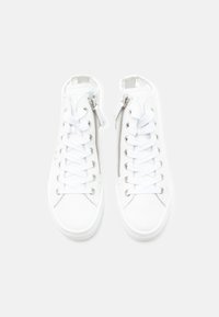 Ζευγάρι λευκών sneakers ψηλού τύπου με πλαϊνά φερμουάρ και λευκά κορδόνια σε φωτεινό φόντο, στο πλάνο από πάνω.