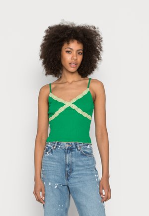 Top de alças verde, canelado, com detalhes de renda leve entrelaçada, alças finas, combinado com jeans rasgados de cintura alta azuis.