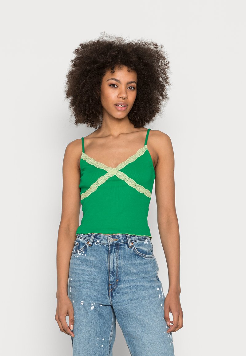 Top de alças verde, canelado, com detalhes de renda leve entrelaçada, alças finas, combinado com jeans rasgados de cintura alta azuis.