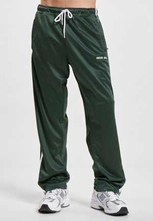 Grønne treningsbukser med hvite sidestriper og hvit snor, brukt med hvite og grå joggesko.