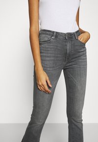 Grå denimjeans med en figursydd design, femfickorsstil och knappstängning. Synlig sömnad och lätt blekning längs benen.