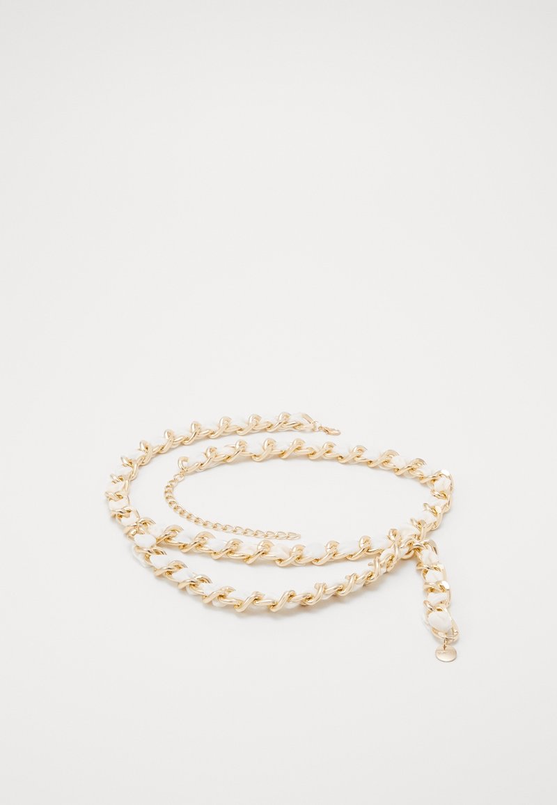 Ceinture en chaîne dorée entrelacée avec un matériau blanc, posée en boucle avec une petite étiquette dorée suspendue sur un fond blanc uni.