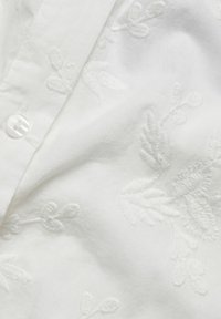 Biała koszula bawełniana z delikatnymi haftowanymi wzorami liści, klasycznym kołnierzykiem i pojedynczym zapięciem na perłowy guzik.