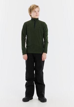 Donkergroen fleecetrekker met een halve rits en zwarte accenten, gecombineerd met zwarte waterdichte broeken en stevige zwarte laarzen. Casual buitensportkleding.