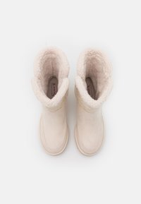Stivali in suede beige con un interno morbido e foderato e risvolti, caratterizzati da trame lisce e una punta arrotondata.