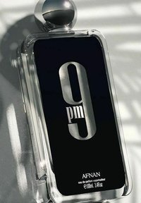 Tydlig rektangulär glasparfymflaska med ett silverlock. Svart etikett med "9 pm" i stor silvrig font. 100 ml kapacitet angiven.