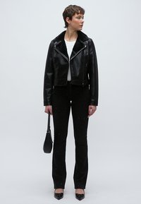 Fekete bőr motoros dzseki műszőrme gallérral, melyhez fekete, enyhén csillogó, szárában bővülő nadrág és hegyes orrú fekete cipő társul.