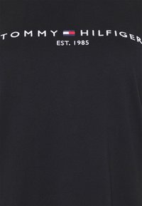 Sort bomulds T-shirt med "TOMMY HILFIGER" og "EST. 1985" i hvid broderi, med et rødt, hvidt og blåt flaglogo mellem ordene.