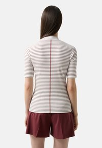 Kortærmet top i hvid med røde vandrette striber, der har en simpel krave og en detalje med en søm bagpå, parret med bordeaux shorts.