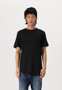 T-shirt noir à manches courtes en coton doux, avec un col rond et un ourlet allongé, porté avec un jean en denim bleu.